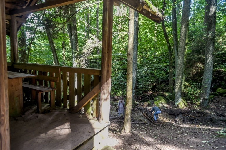 Zwei Kinder spielen im Bayrischen Wald. Im Vordergrund ist eine kleine Holzhütte zu erkennen.