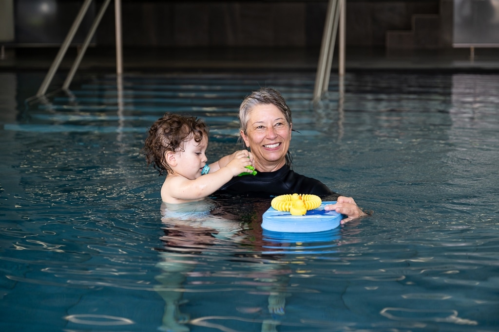 Schwimm- und Saunameisterin Pia Fax steht in einem Pool und hält ein Kind auf dem Arm