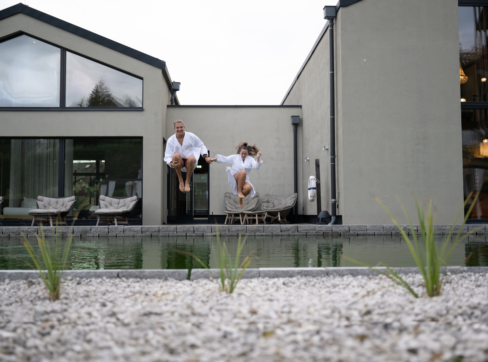 Ein junges Paar in weißen Bademäntel springt in einen Pool